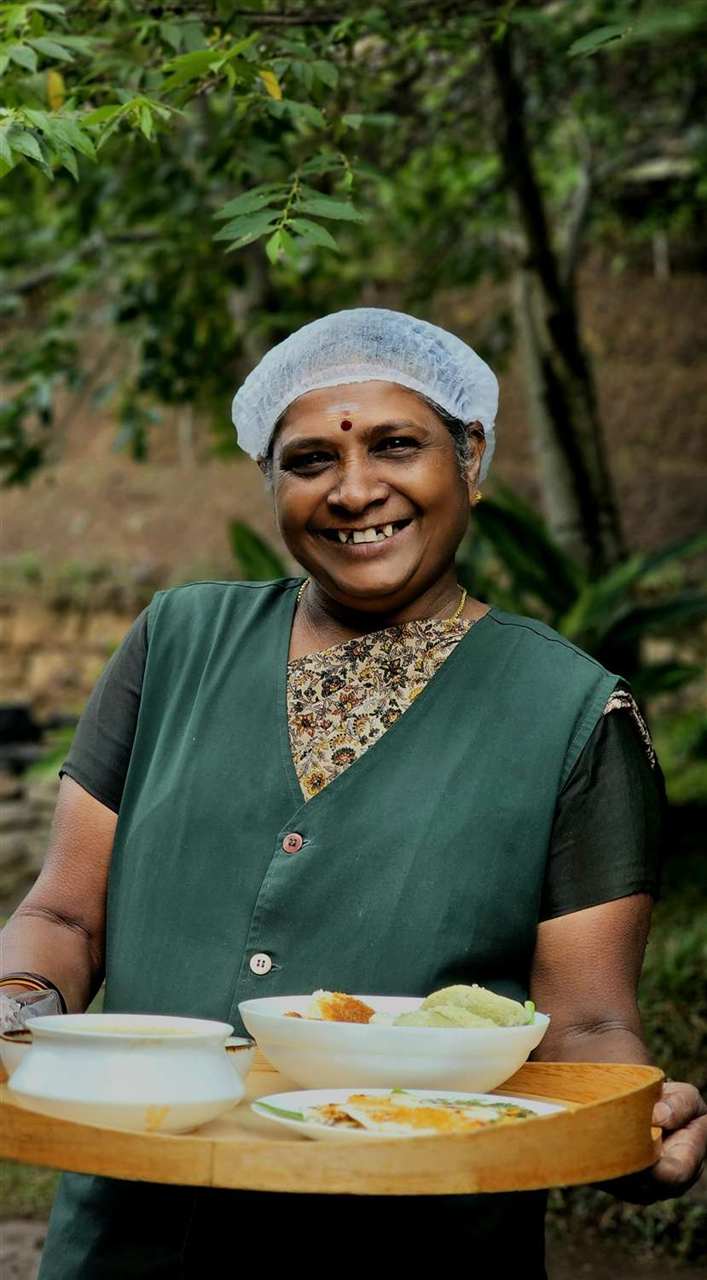 A smiling host carrying a breakfast tray of idli and chutney